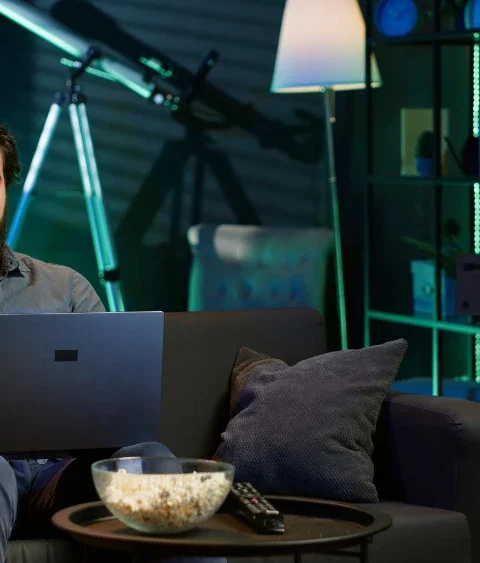 Homem assistindo filmes que todo amante de tecnologia deve assistir, com ambiente de tecnologia, iluminação de LED e um laptop no sofá.