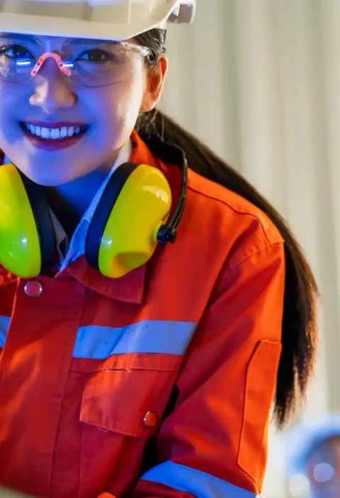 Mulher engenheira usando tecnologia vestível de proteção no trabalho, com capacete, óculos de proteção e protetores auriculares, em ambiente industrial