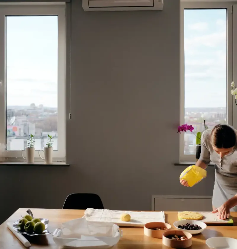 A mulher preparando alimentos na cozinha de um apartamento com janelas grandes que promovem ótima ventilação e iluminação natural, ideal para escolher o melhor tipo de janela.
