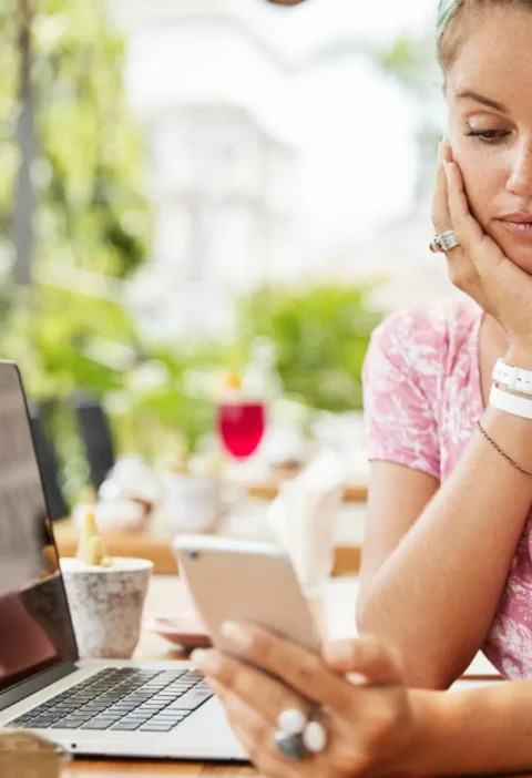 Mulher em ambiente externo usa um laptop e celular, concentrada enquanto consulta informações no dia a dia, representando Comportamento Digital: Como as Pessoas Estão Mudando a Forma de Consumir Informação.