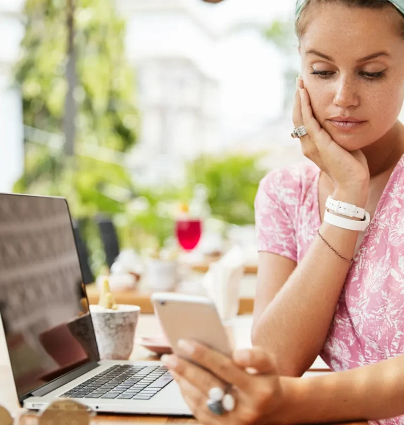 Mulher em ambiente externo usa um laptop e celular, concentrada enquanto consulta informações no dia a dia, representando Comportamento Digital: Como as Pessoas Estão Mudando a Forma de Consumir Informação.