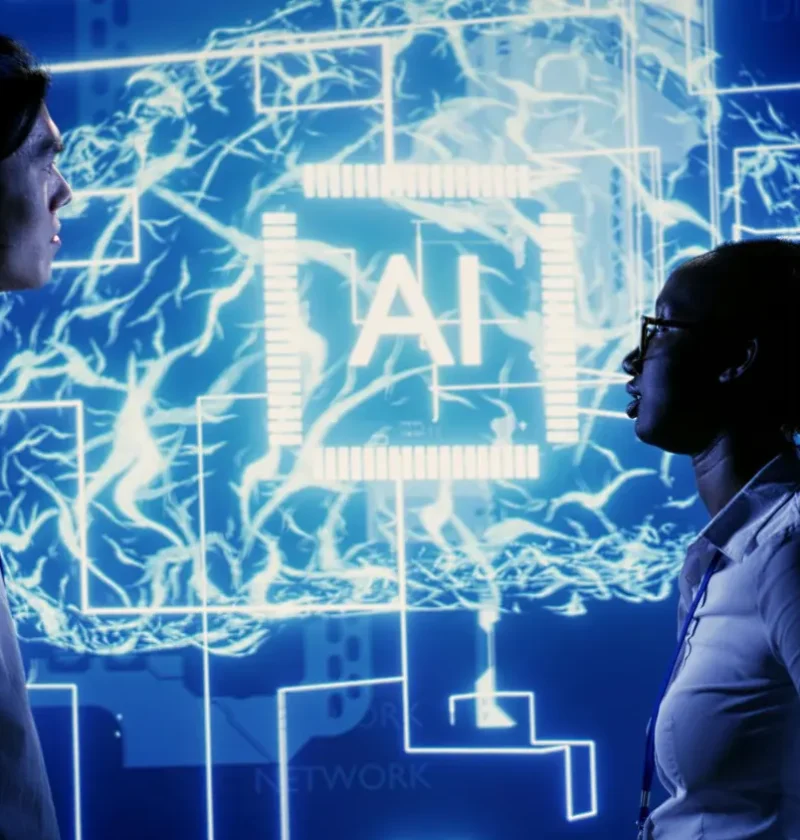 Cena de dois profissionais em silhueta conversando diante de um painel holográfico com símbolos de IA e circuitos digitais, simbolizando Inteligência Artificial: Como a tecnologia está mudando diferentes profissões.